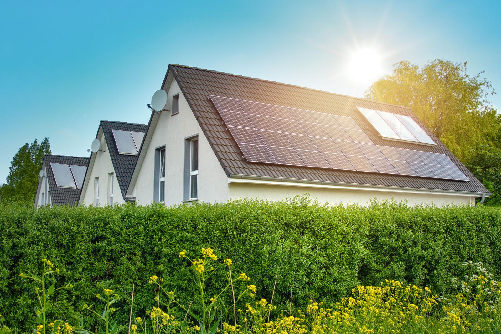 Reihe von Häusern mit Solarpaneelen und Dachflächenfenstern auf dem Ziegeldach im Sonnenlicht
